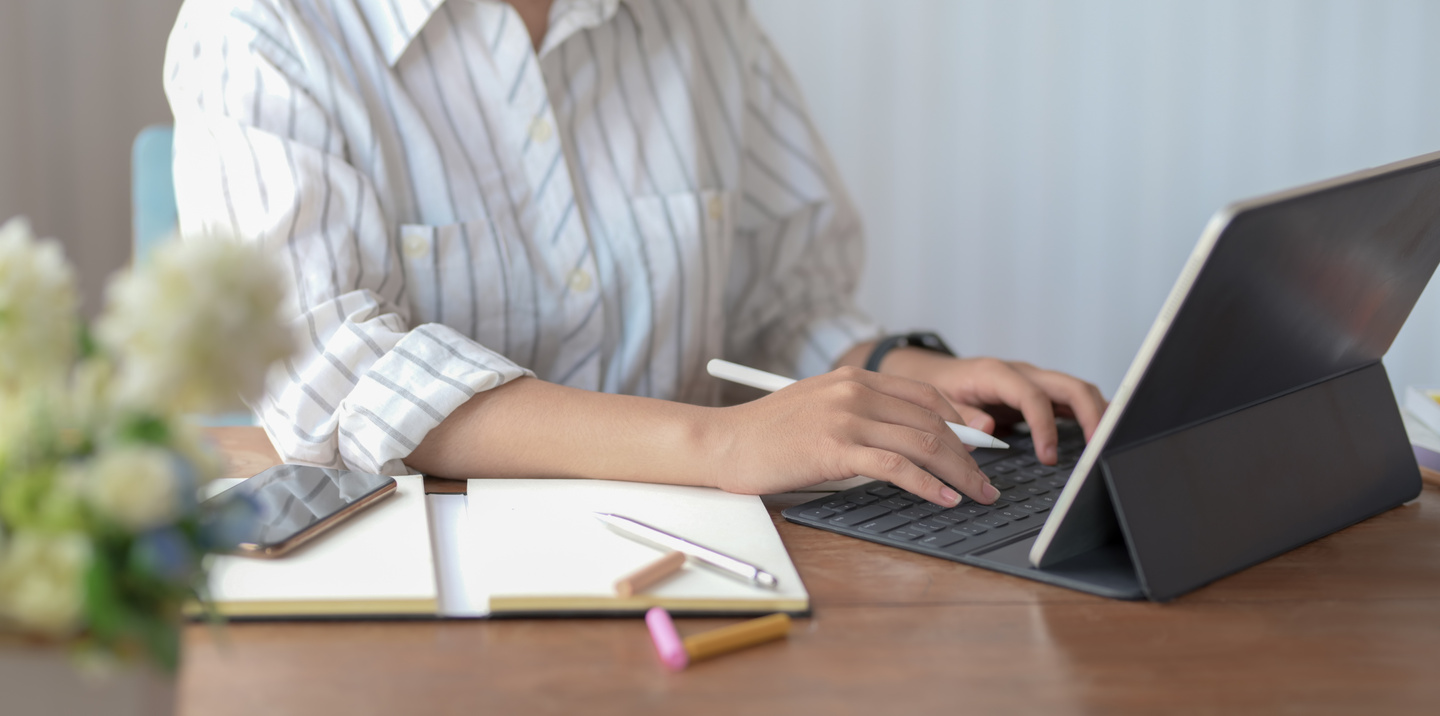 Close-up Photo of Person in White Shirt Sitting at a Table Using a Laptop